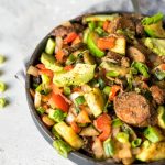 A plate of chopped veggies with avocado and vegan sausage slices.