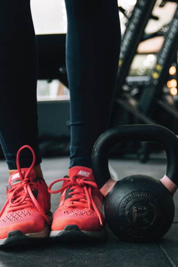 The lower half of someone's legs in running shoes standing beside a kettlebell.