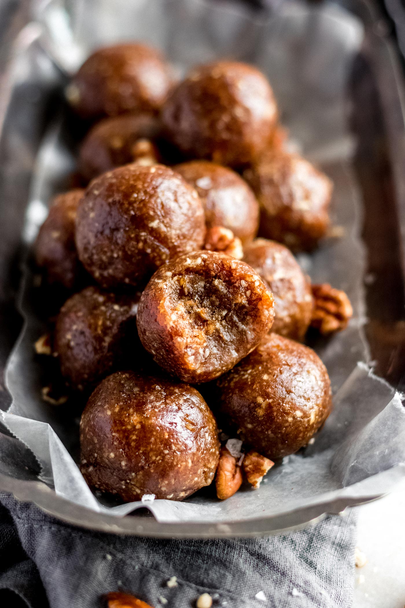 A serving plate of pecan pie balls made from blended pecans and dates. One ball on top has a bite out of it.