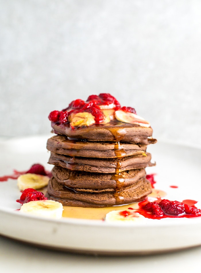 A stack of chocolate pancakes topped with raspberry and banana.
