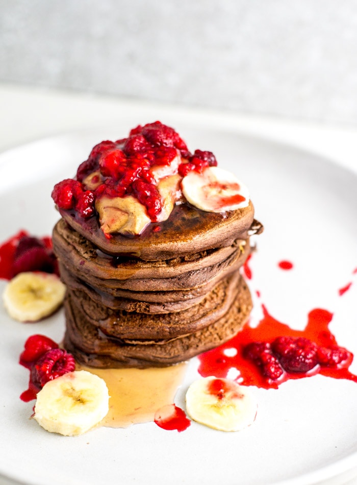 A stack of chocolate protein pancakes topped with syrup, berries and banana.