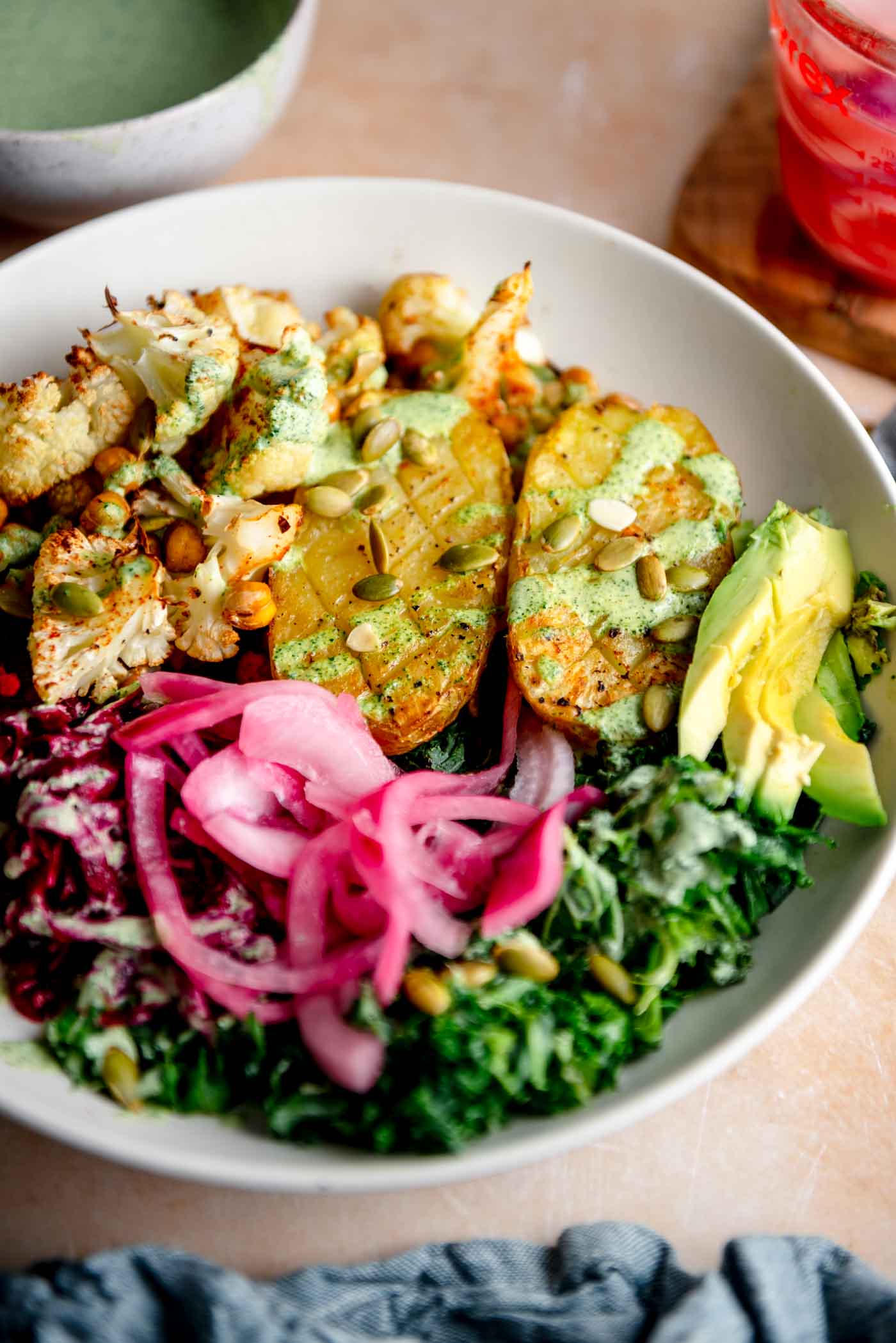 Bowl with a baked potato, chopped roasted cauliflower and chickpeas, kale, pickled red onion, shredded beets, and creamy green dressing drizzled over top.