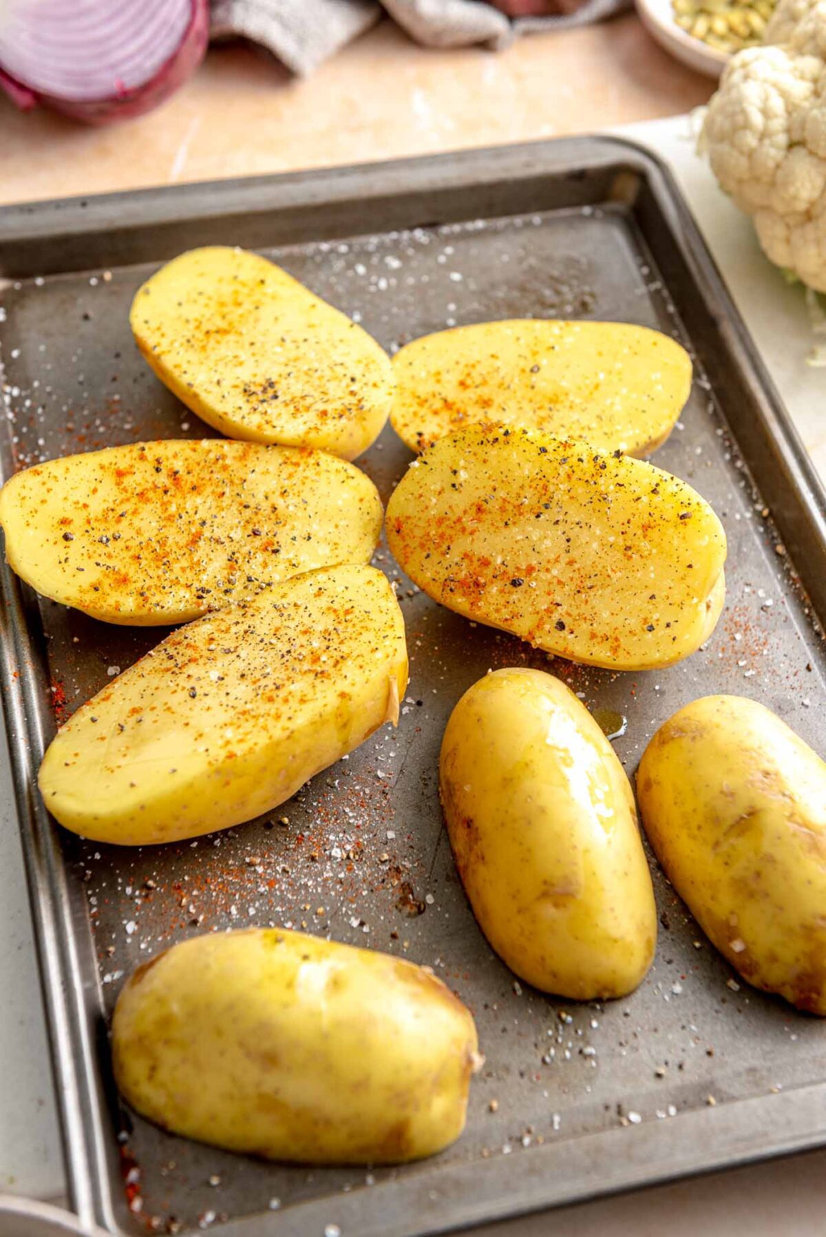 Halved Yukon Gold potatoes sprinkled with spices on a baking sheet.