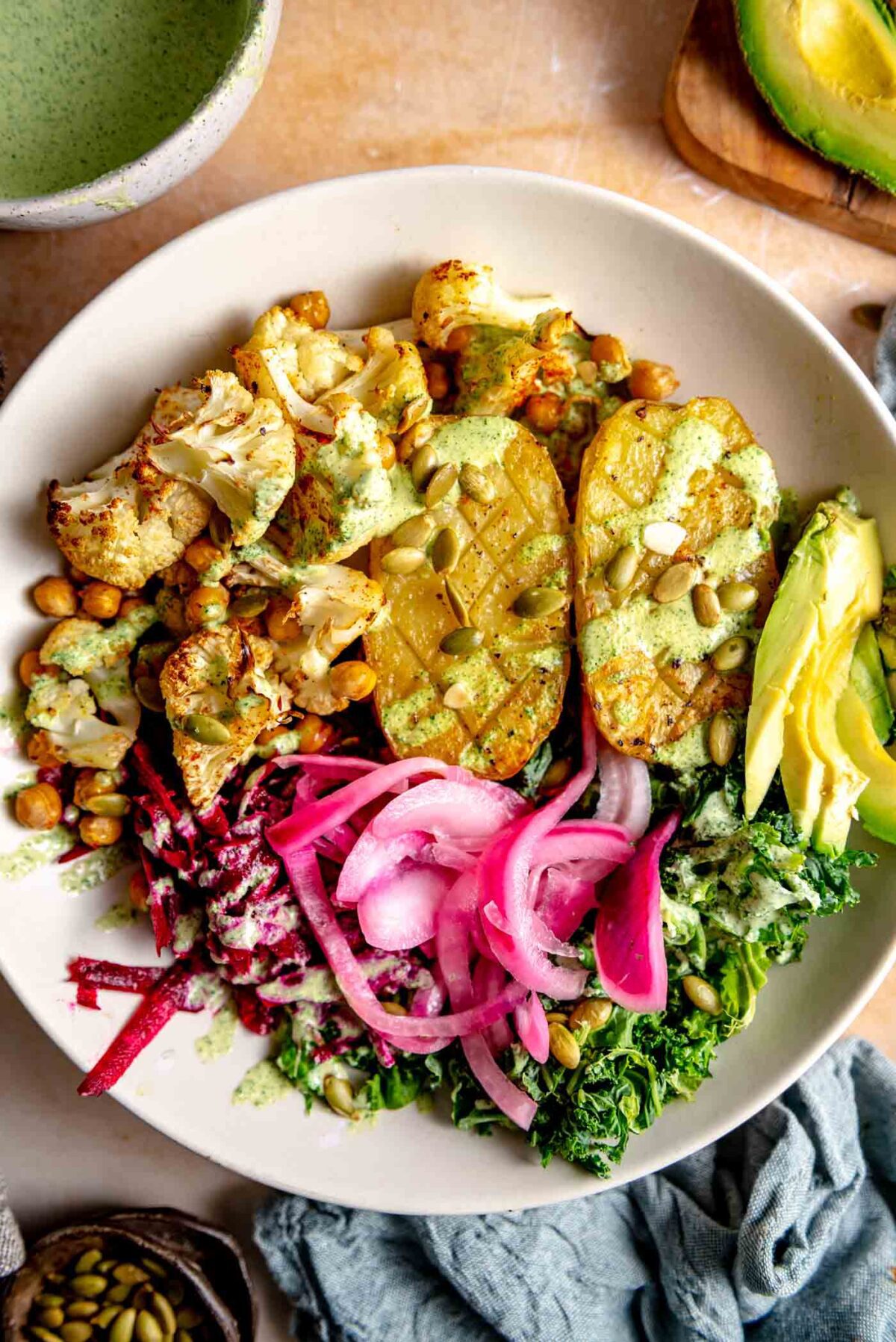 Bowl with a baked potato, chopped roasted cauliflower and chickpeas, kale, pickled red onion and creamy green dressing drizzled over top.