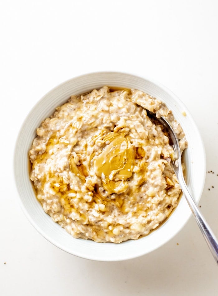 Overhead view of a bowl of banana chia oatmeal topped with peanut butter and maple syrup. A spoon rests in the bowl.