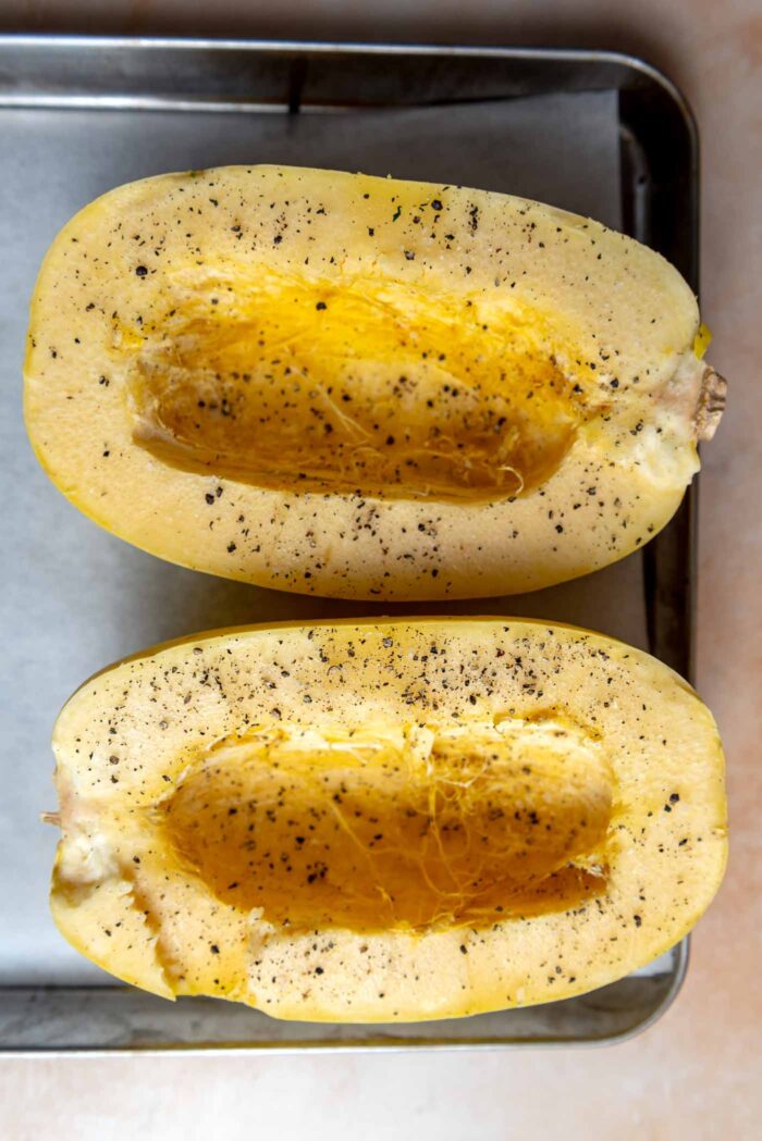 Two halves of a spaghetti squash with seeds removed and sprinkled with salt and pepper.