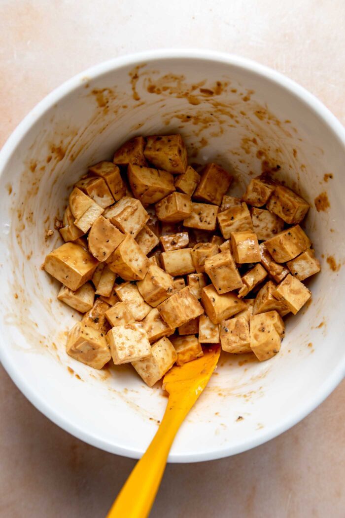 Cubed tofu mixed with soy sauce in a bowl with a small spatula resting in it.