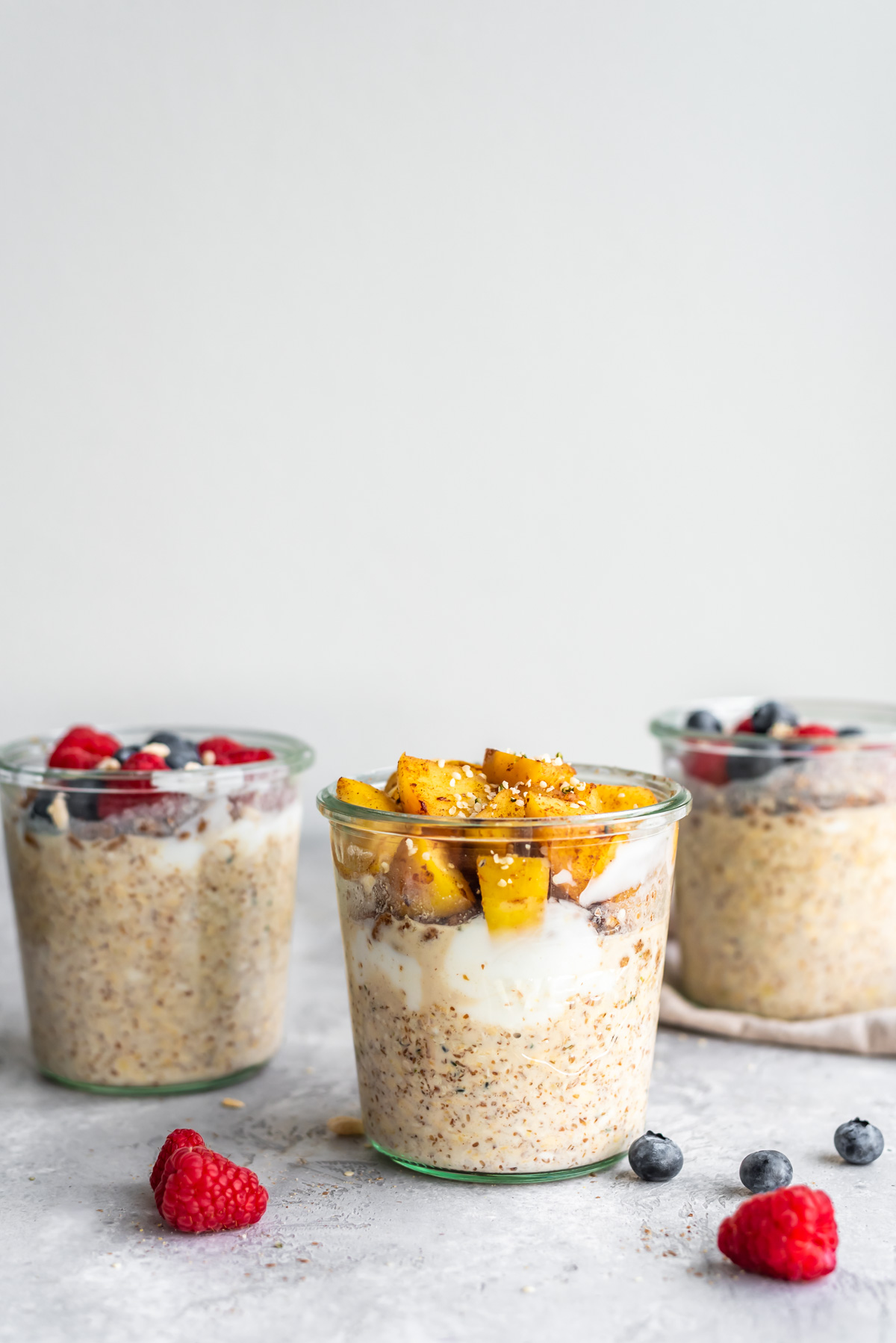3 jars of overnight oats with different toppings like stewed apples and fresh berries.