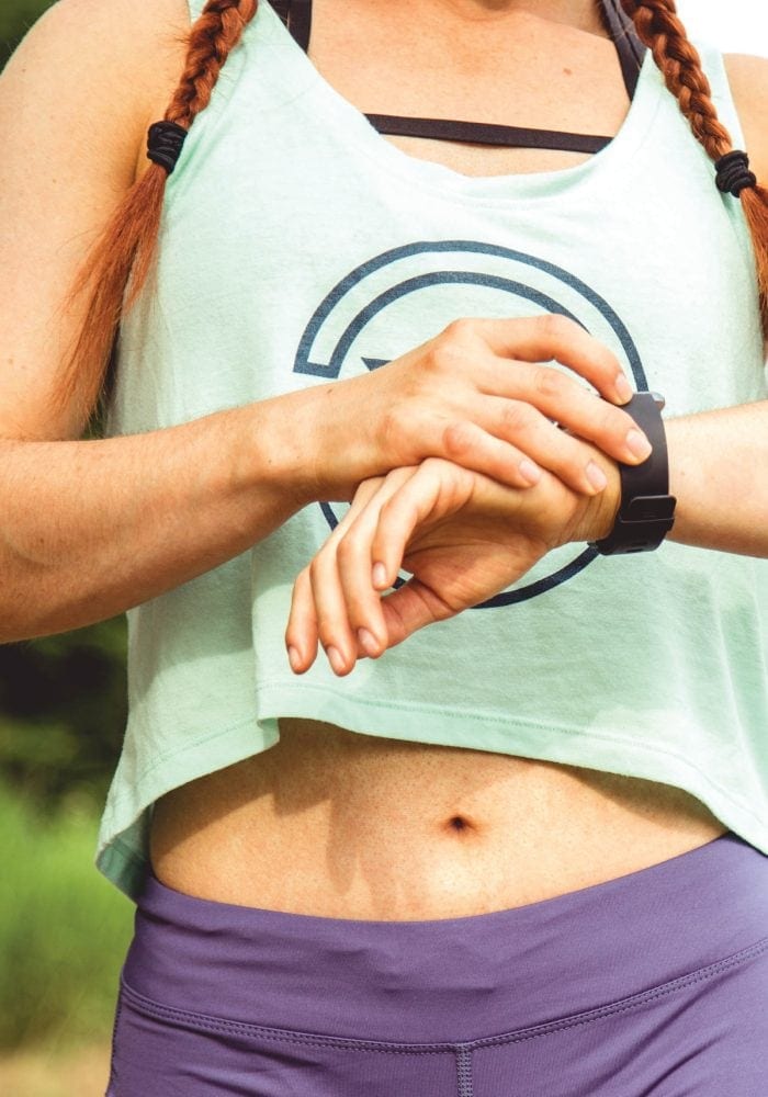 Fit woman in a green crop top checking her watch.