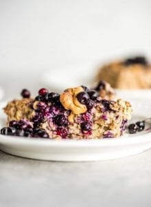 A slice of baked banana oatmeal topped with berries and peanut butter on a plate.