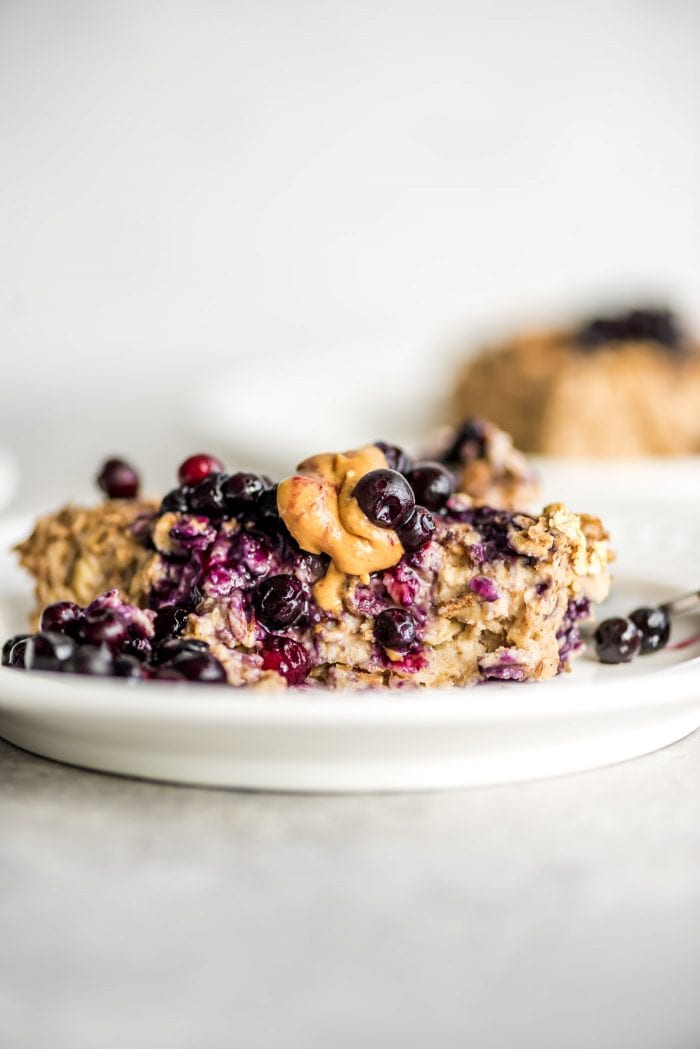 Banana baked oatmeal on a small white plate topped with berries and peanut butter.