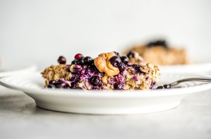 Close up of a slice of baked oatmeal with blueberries and peanut butter on a white plate.