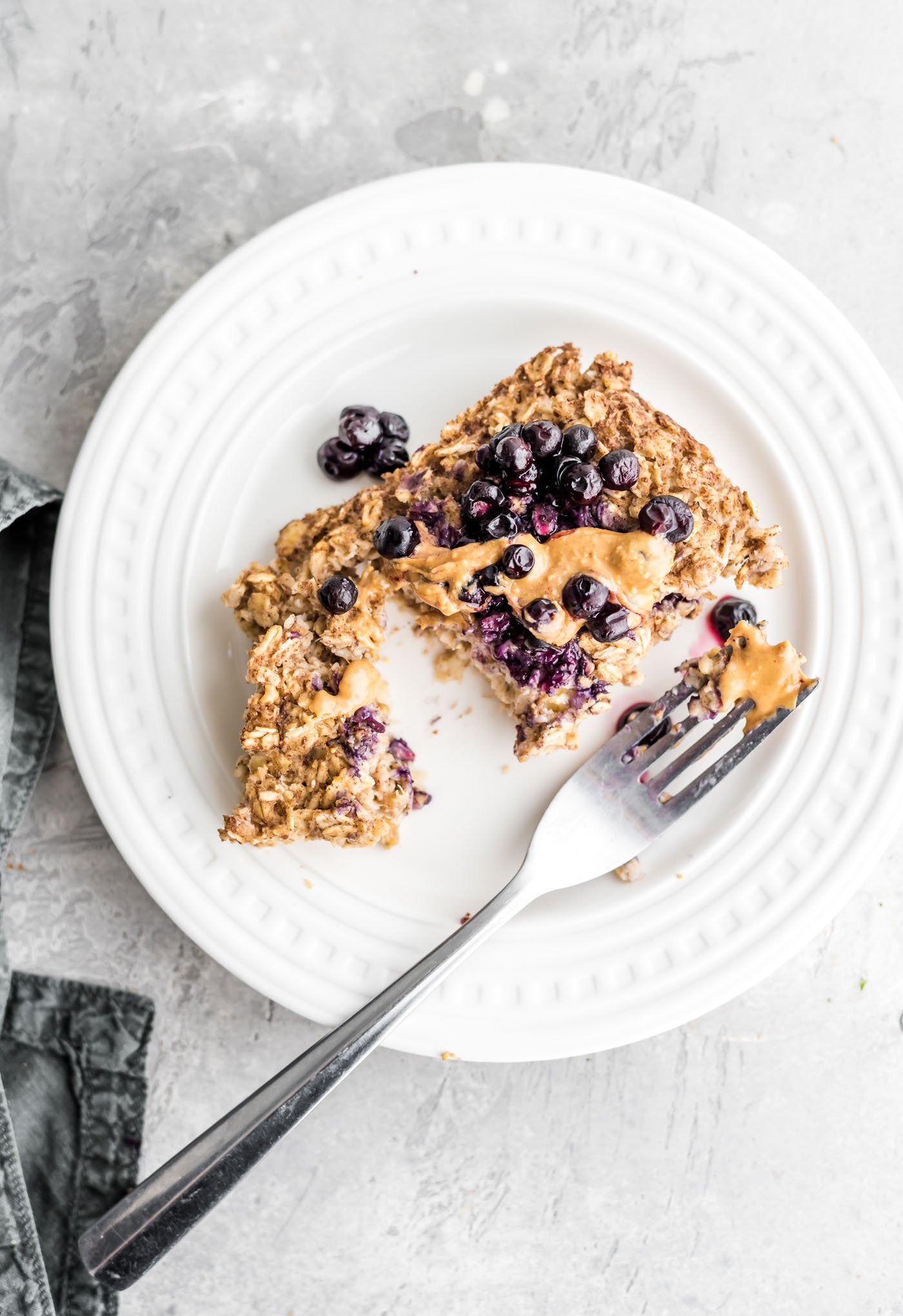 A slice of baked banana oatmeal topped with peanut butter and berries on a plate.