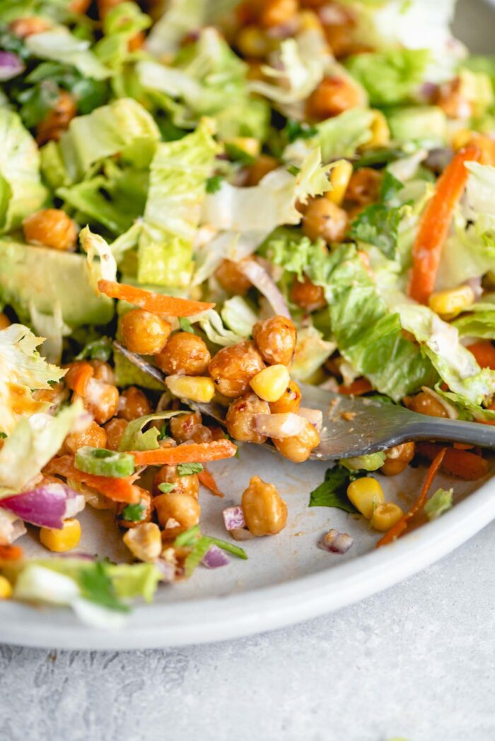 Close up of a fork of BBQ chickpea salad with red onion, green onion, lettuce, carrot and corn.