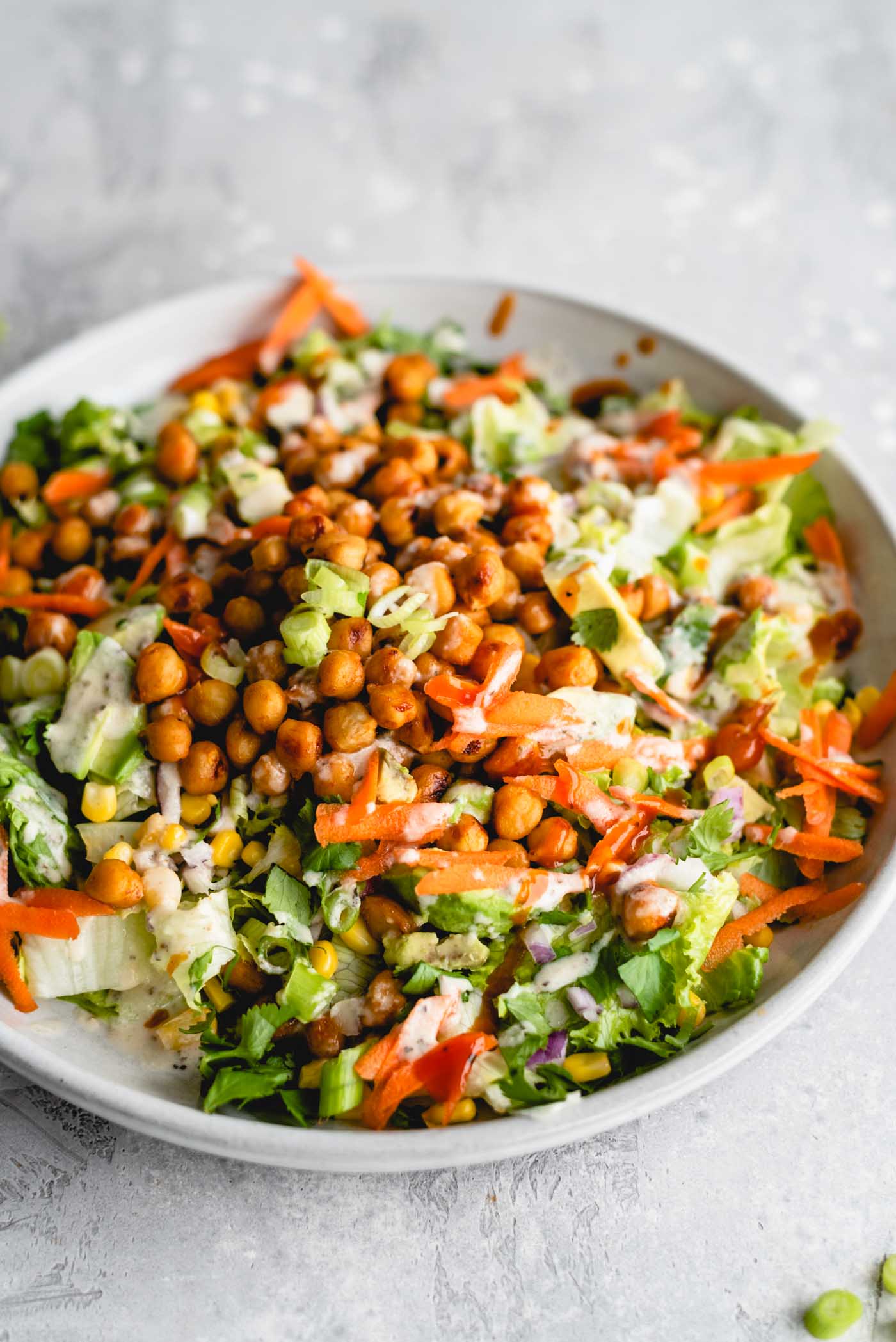 BBQ chickpea salad with lettuce, carrot, avocado, corn and tahini ranch dressing on a plate.