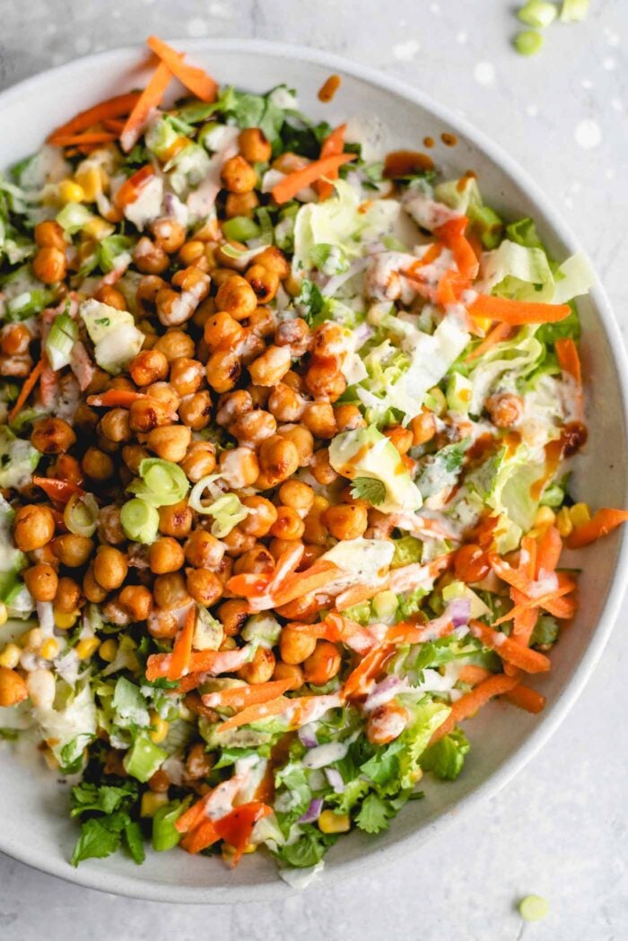 Overhead view of a plate of BBQ chickpea salad with tahini sauce, carrot, corn, cilantro, avocado and carrot.