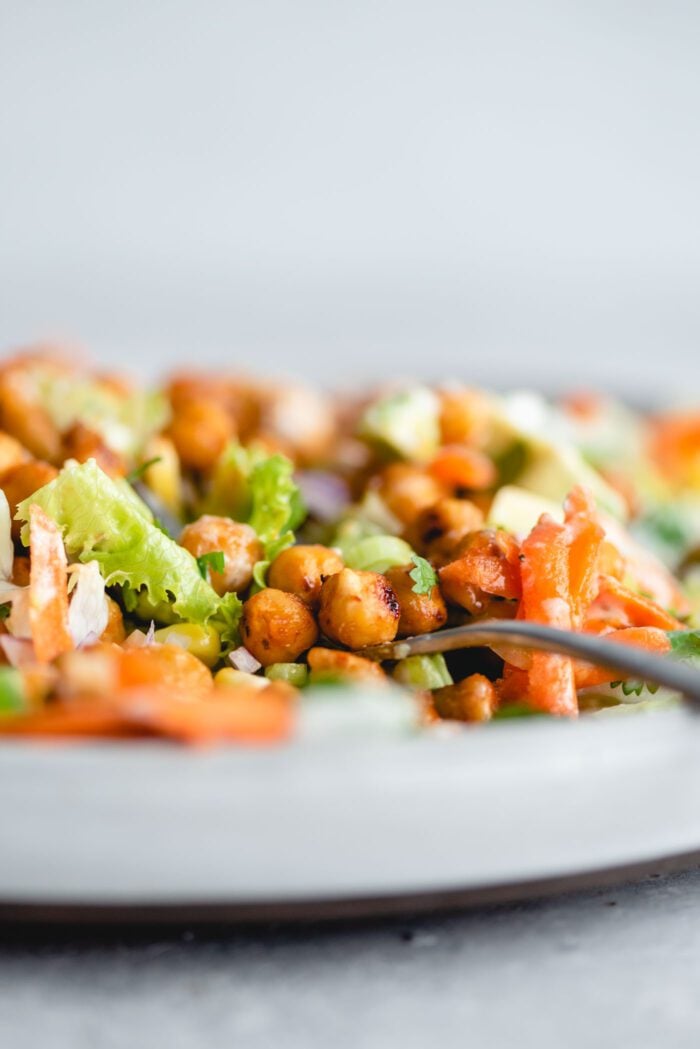 Close up of a few BBQ chickpeas sitting on a fork on a plate of BBQ chickpea salad with lettuce, corn and carrot.