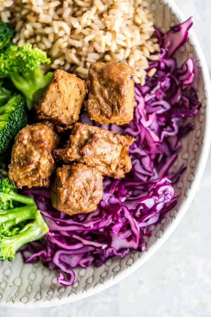 Marinated baked tempeh in a bowl with red cabbage, broccoli and brown rice.