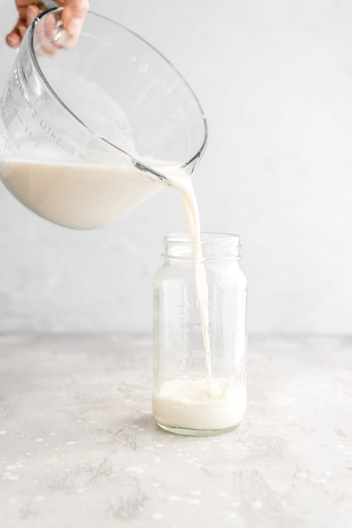 Pouring healthy, creamy homemade oat milk into a mason jar for storing.