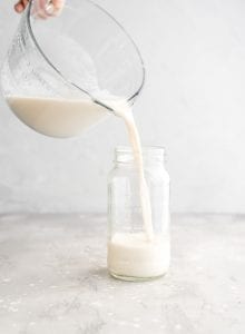Pouring a homemade oat milk recipe into a glass storage container.