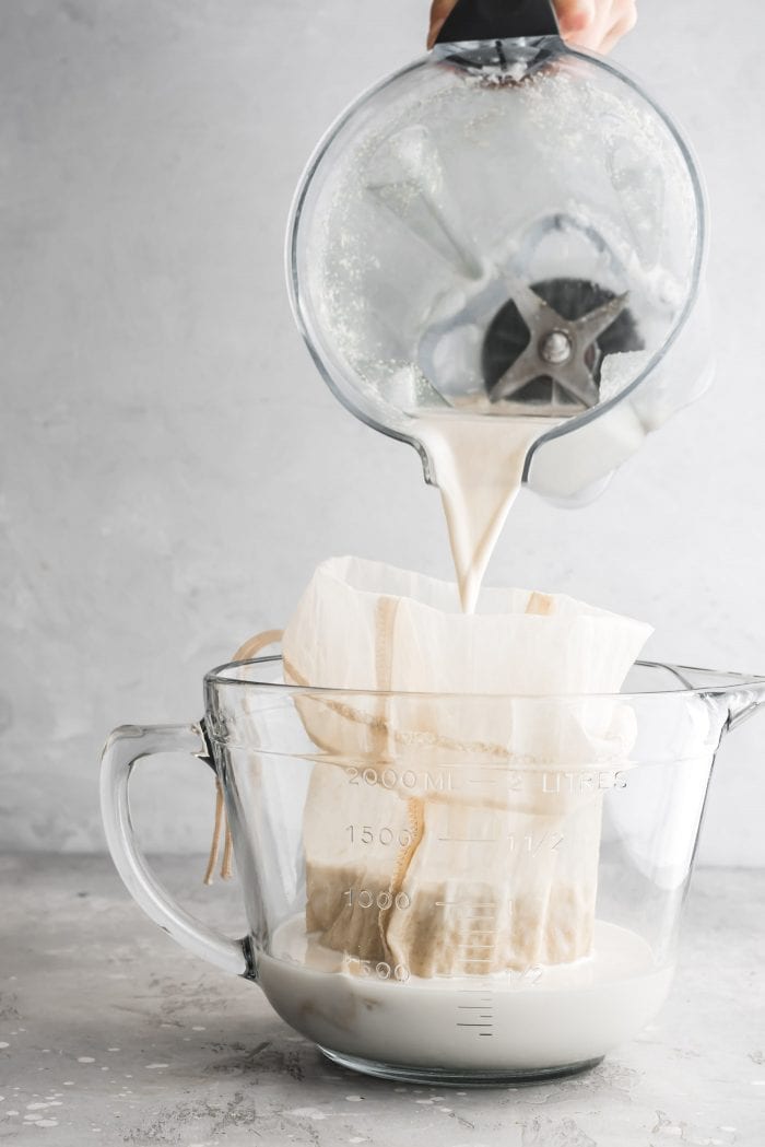 Pouring blended homemade oat milk into a nut milk bag in a measuring cup.