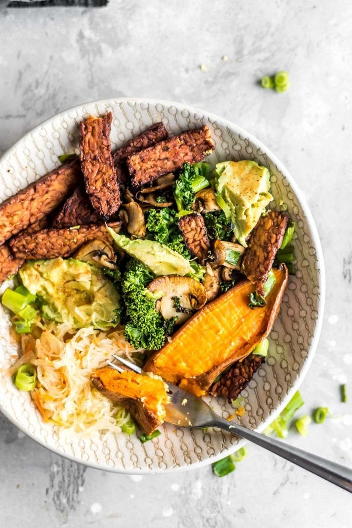 Cooked tempeh bacon, avocado, roasted sweet potato, sauerkraut, kale and mushrooms in a breakfast bowl.