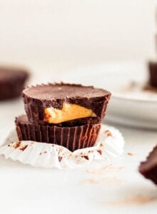 Stack of 2 chocolate peanut butter cups, one has a bit out of it to show inside. More cups in background.