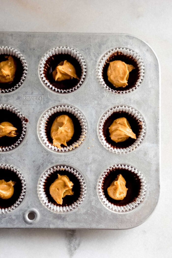 Dollops of peanut butter spooned into a lined muffin tin.