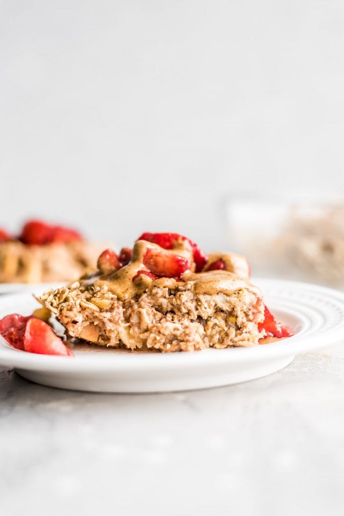 A square of apple baked oatmeal topped with almond butter and strawberries on a plate.