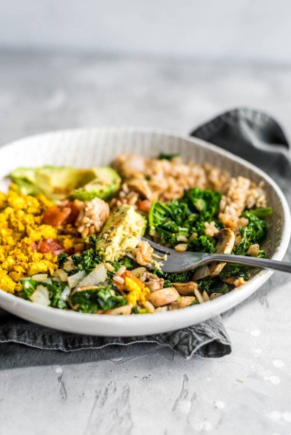 Avocado in a savory vegan breakfast bowl with kale, tofu scramble, rice and salsa.