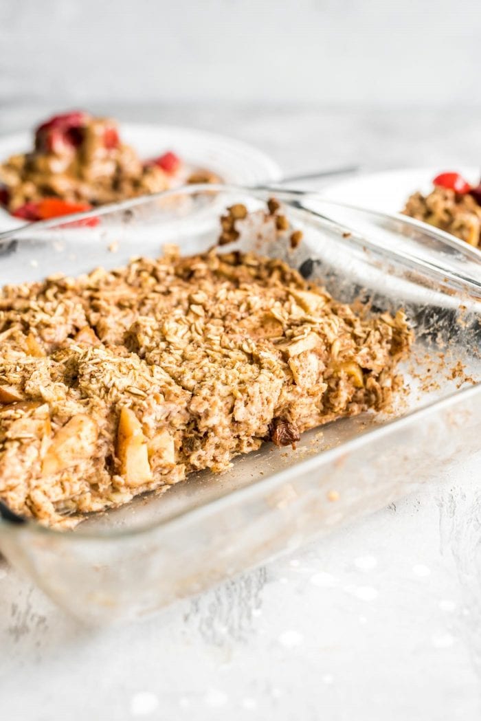 Apple cinnamon baked oatmeal in a glass baking dish with two portions removed and on plates in the background.