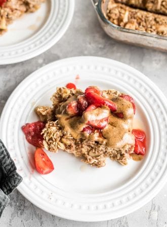 A portion of baked apple cinnamon oatmeal on a plate topped with almond butter and strawberries.