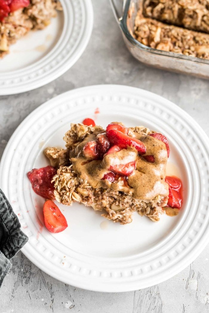 A portion of baked apple cinnamon oatmeal on a plate topped with almond butter and strawberries.