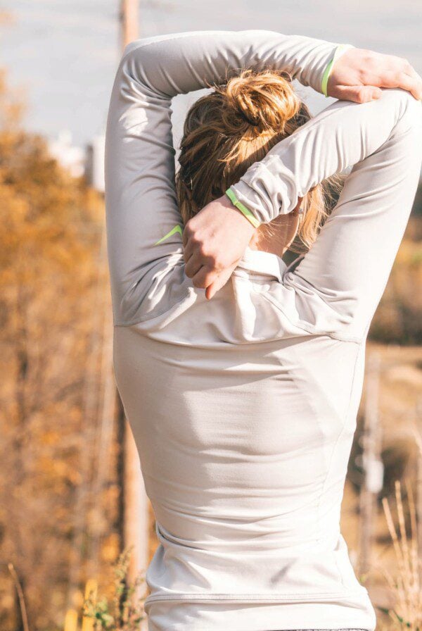 Women in a white Nike jacket performing a tricep stretch.