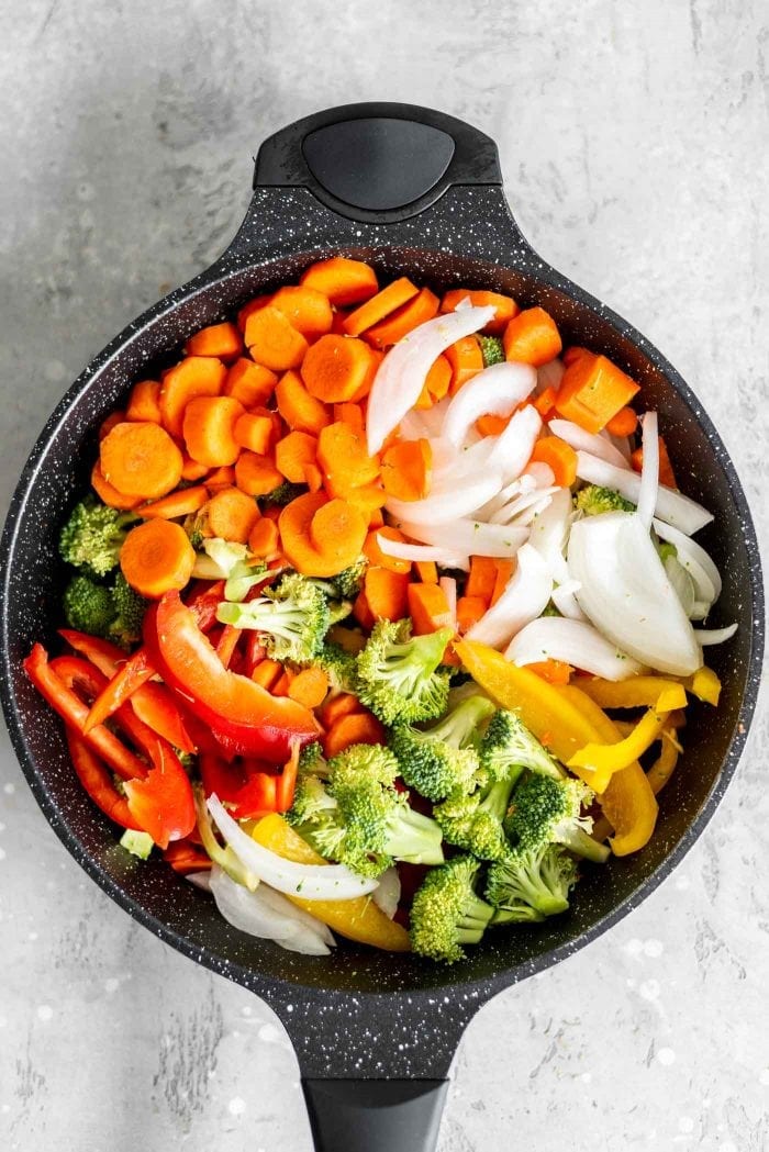 Peppers, broccoli, onions and carrot in a black skillet.