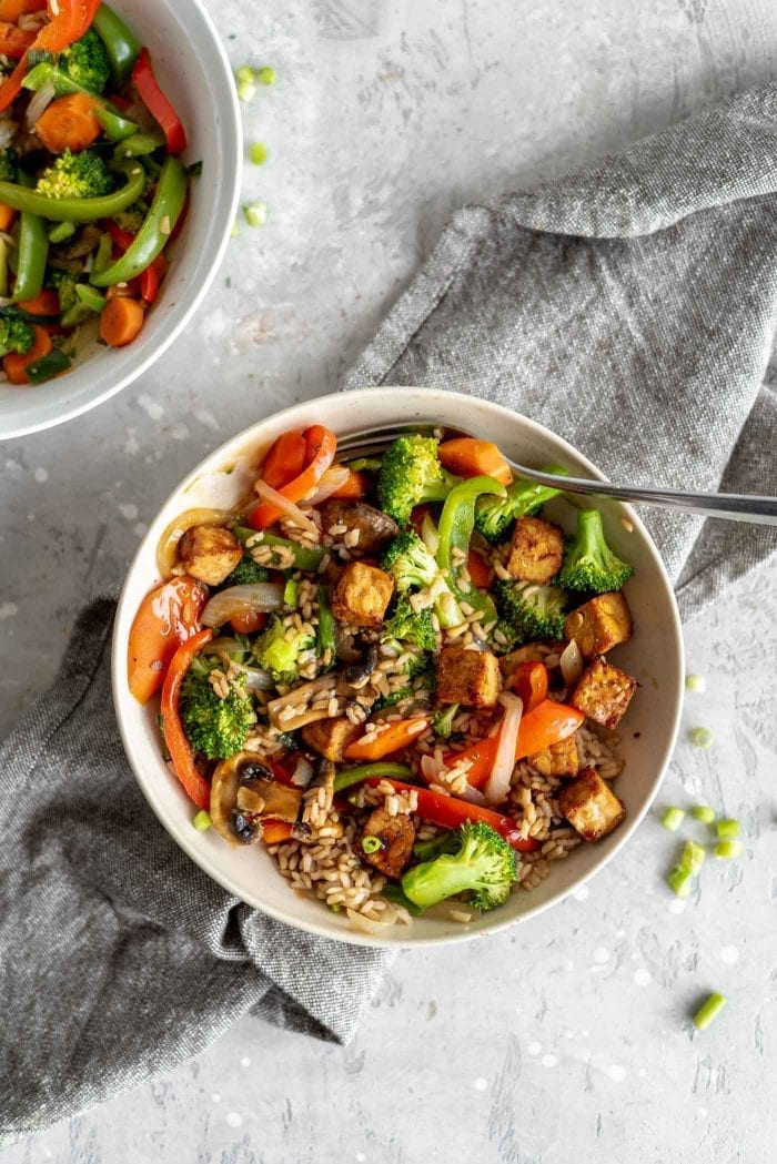 Mixed stir fry veggies with brown rice and tempeh in a bowl.