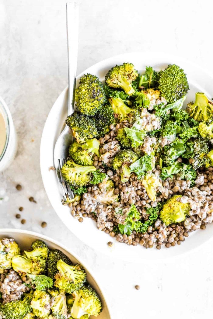 French lentils with massaged kale and roasted broccoli in a bowl with tahini sauce.