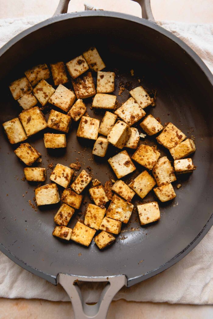 Tofu cubes coated in spices cooking in a pan.