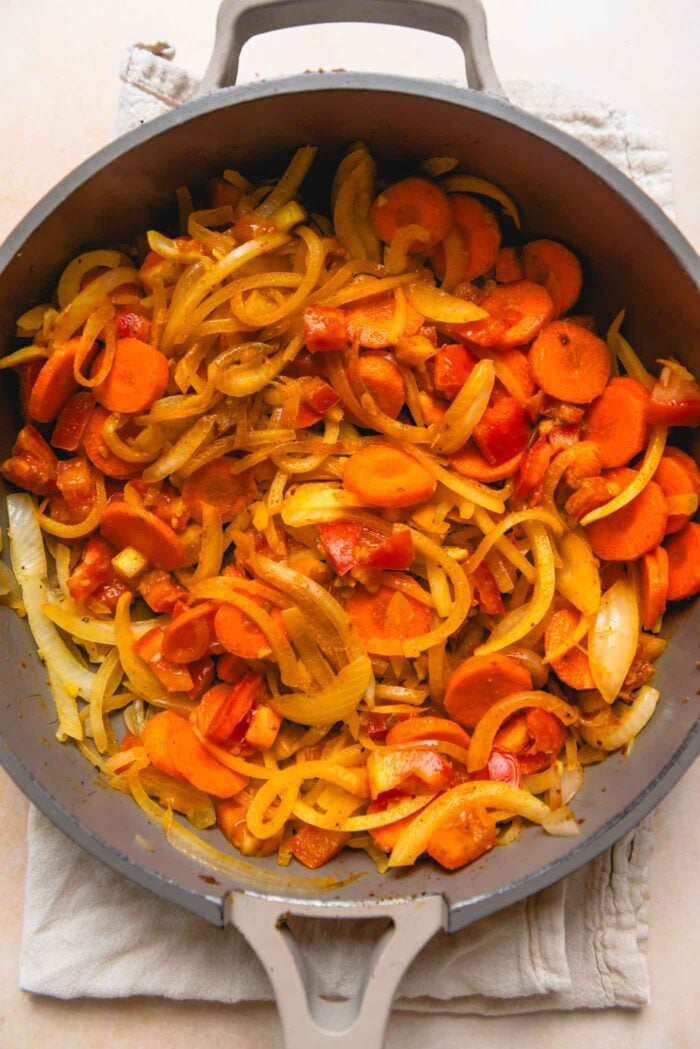 Sliced onion, carrot and bell pepper cooking in a pan.