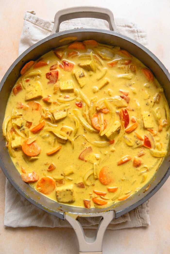 Creamy coconut curry with chopped carrot, onion and bell pepper cooking in a pan.