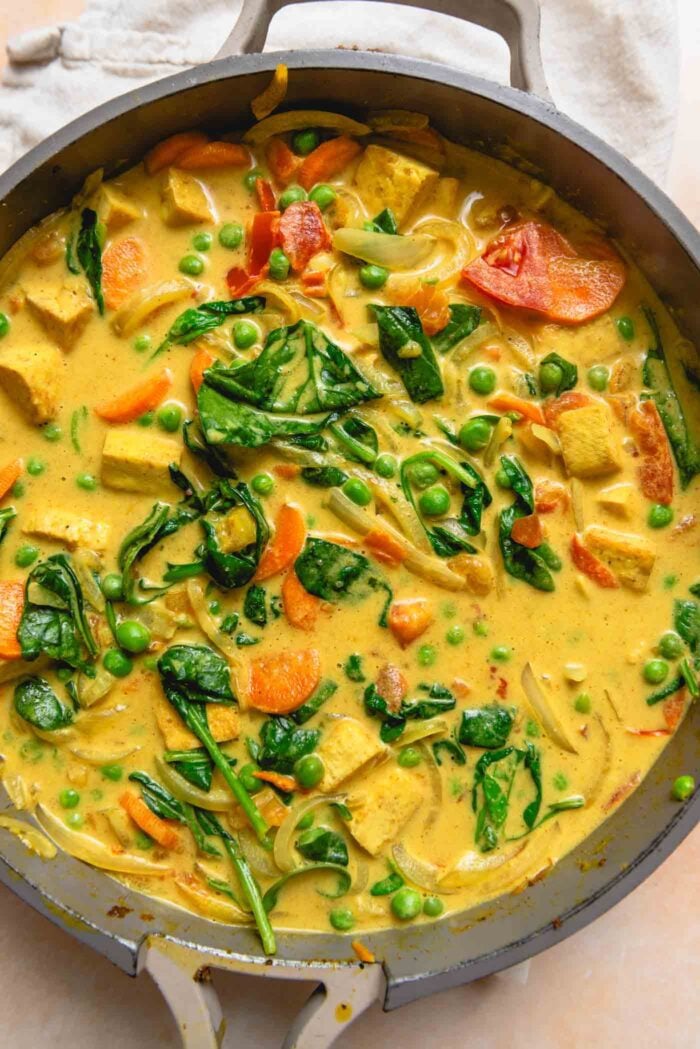 Creamy vegetable coconut curry with tofu cubes, spinach and vegetables cooking in a pan.