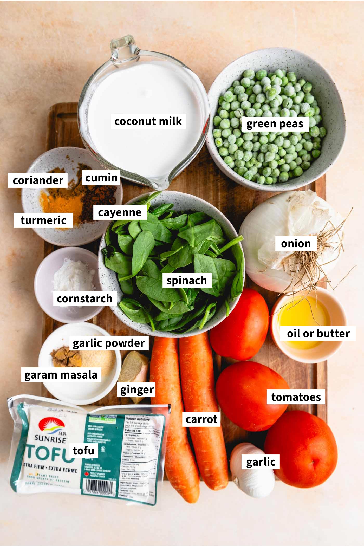 Assorted ingredients laid out for a vegan curry recipe, including carrot, tomato, coconut milk, green peas, and tofu cubes.