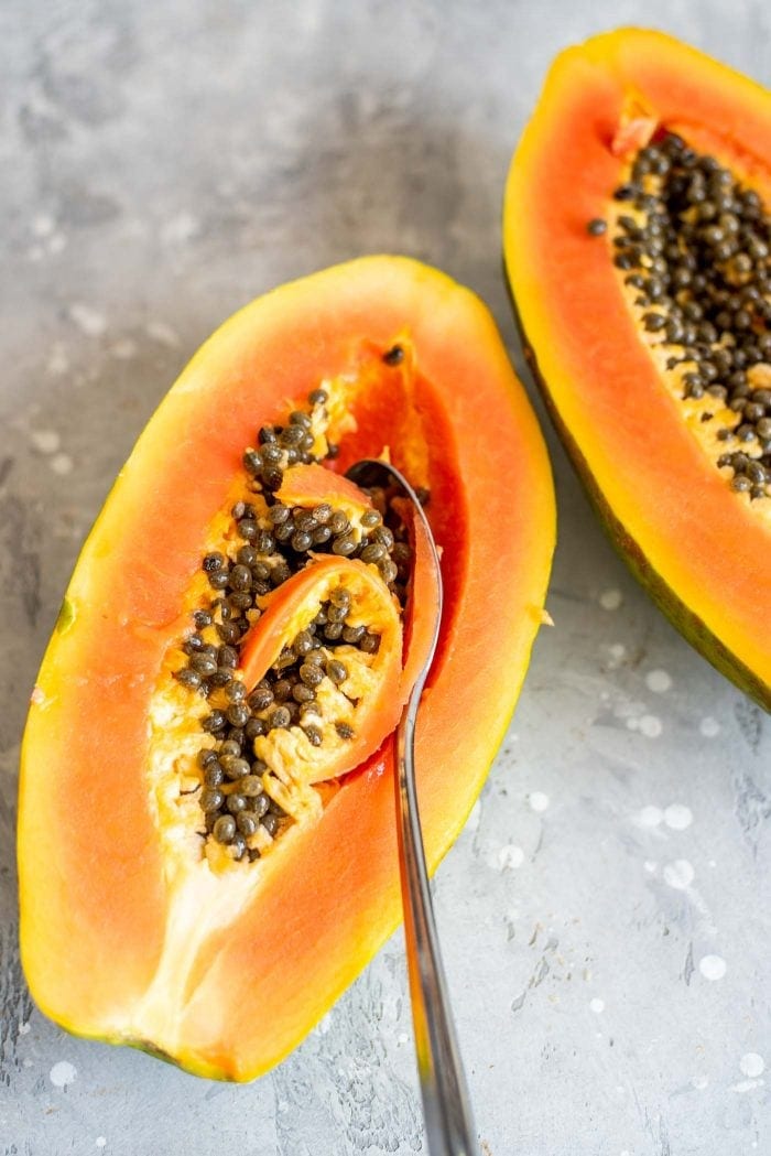 Spoon scooping the seeds out of a papaya.