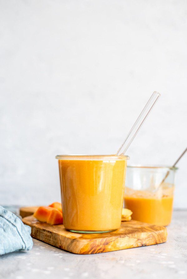 Healthy Creamy Vegan Papaya Smoothie on a cutting board with some chopped pieces of papaya.