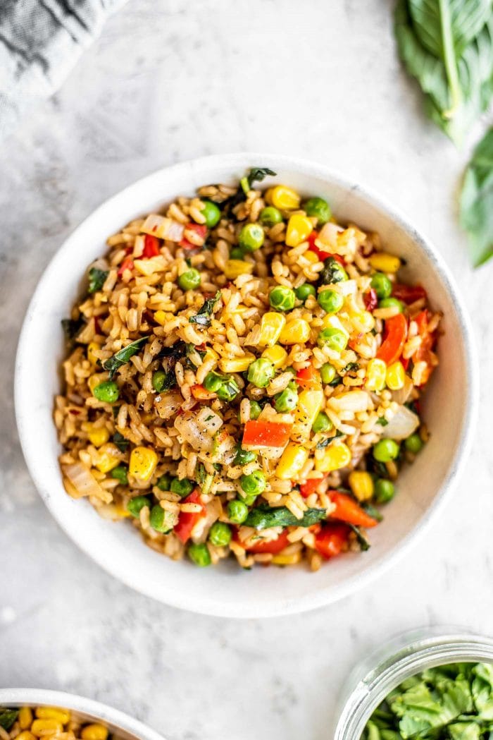 A white bowl filled with vegan basil fried rice with peas and corn.