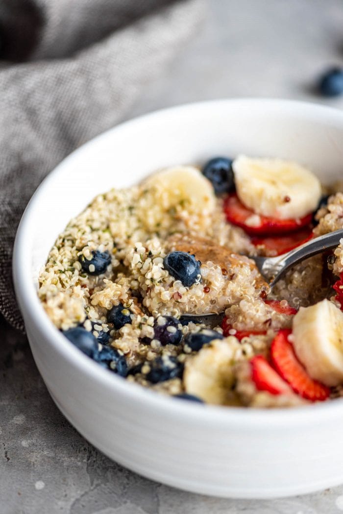 Easy breakfast quinoa in a white bowl with hemp seeds, almond butter, berries and banana.