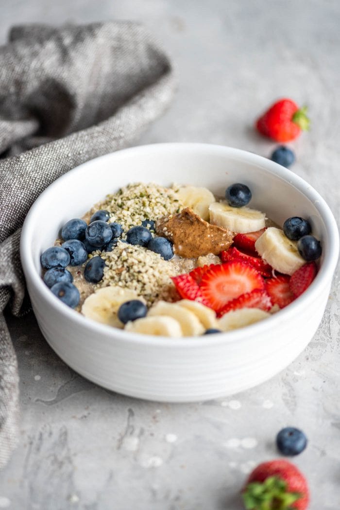 Hot breakfast quinoa in a white bowl with berries, almond butter and banana.