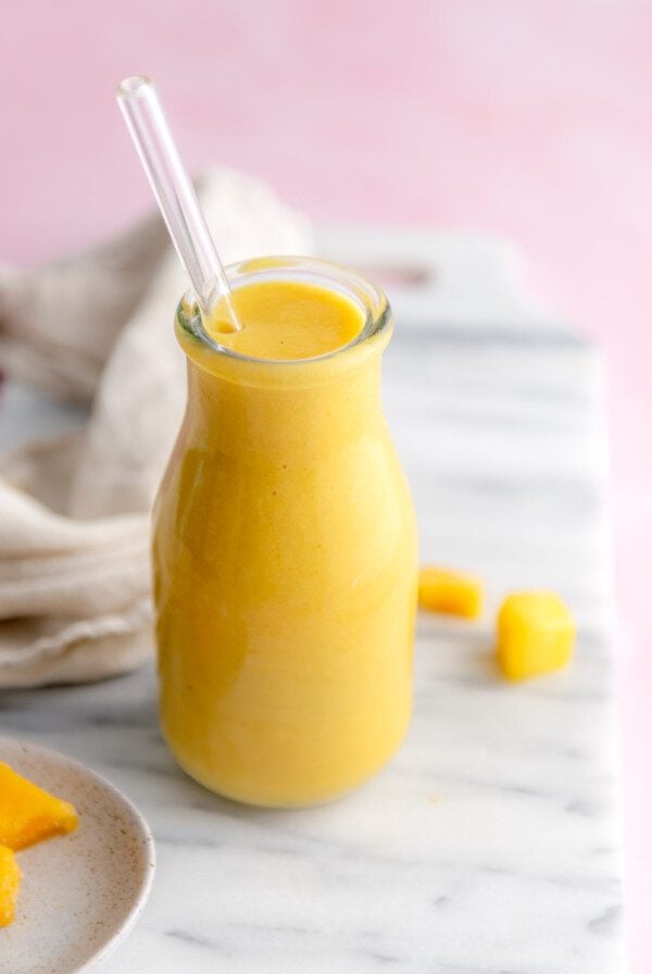 Mango orange smoothie in a glass milk jar with a glass straw in it.