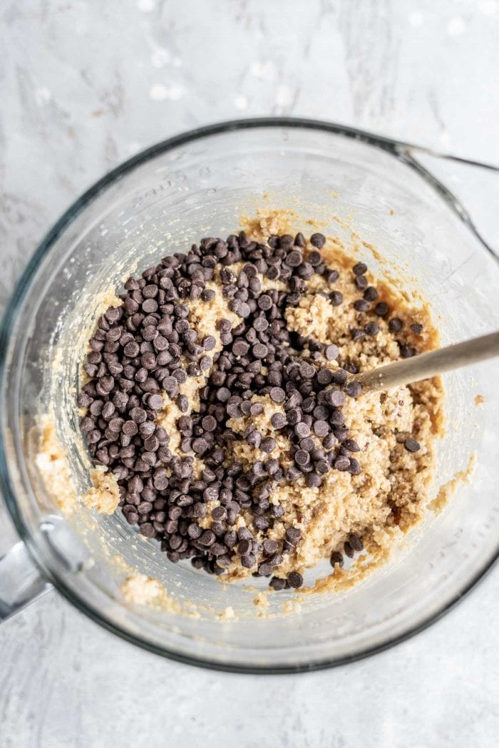 Quinoa cookie dough with chocolate chips in a mixing bowl with a wooden spoon.