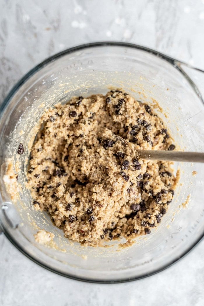 Mixed chocolate chip quinoa cookie dough in a glass mixing bowl with a wooden spoon.